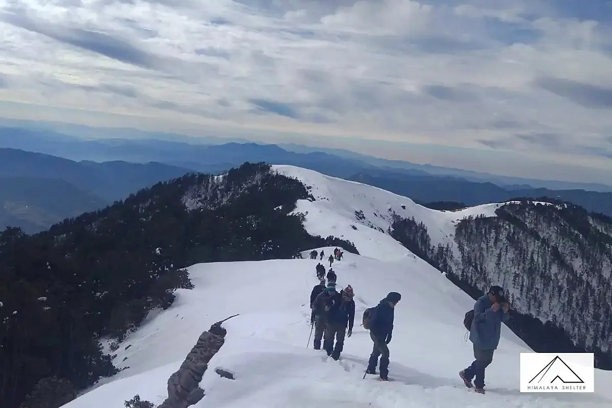 Trekkers dressed in winter layers on a snow-covered ridge of the Brahmatal trek