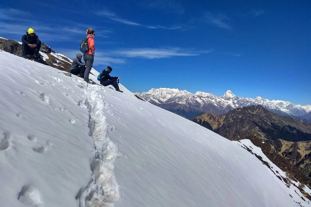 Trekkers resting on a snow slope near Kuari Pass top, where the winter temperature feels coldest in the wind