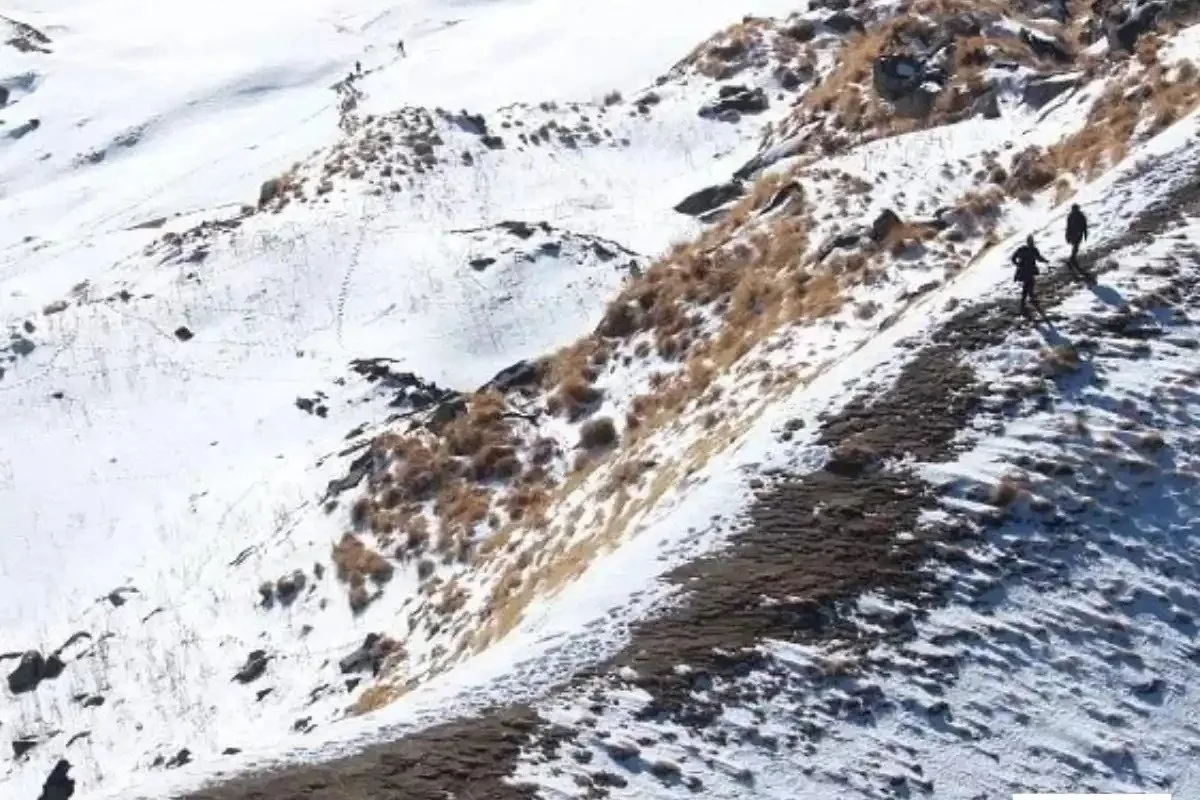 Snow-covered slopes and trekkers on the trail, showing the snowfall season at Kuari Pass