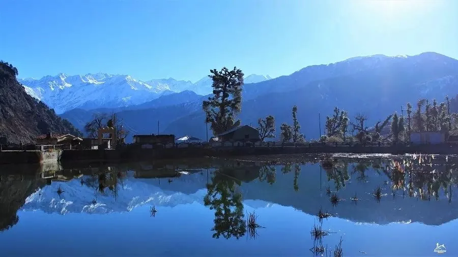 Snow peaks reflected in the lake at Barsu village, the start of the 3-day Dayara Bugyal trek, on a clear and sunny day