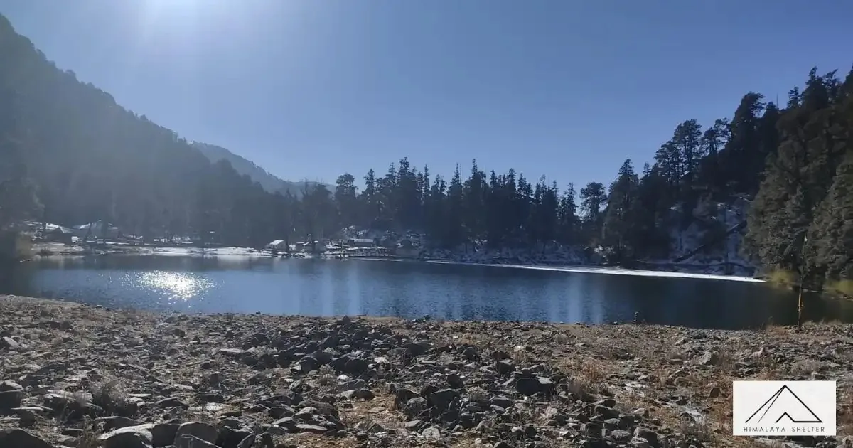 Dodital Lake on a clear day with a rocky shore and dense forest around it