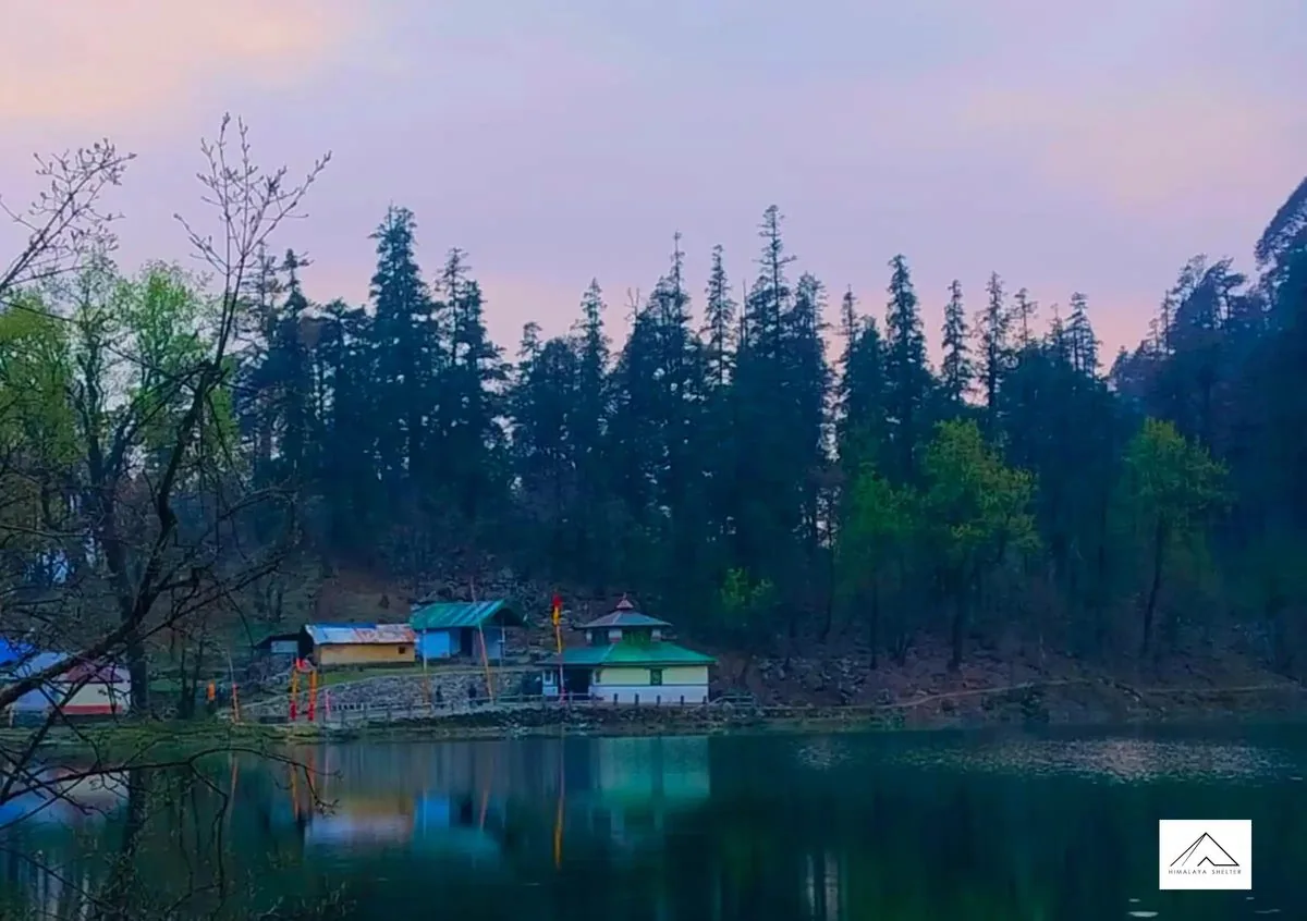 Dodital Lake at dusk with colourful buildings on the far shore and tall forest behind