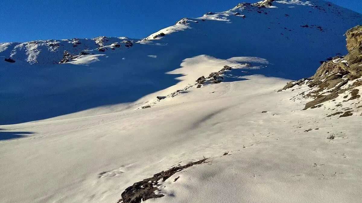 Wide snow slope rising to Kedarkantha peak under a clear blue sky, the steep final climb of summit day