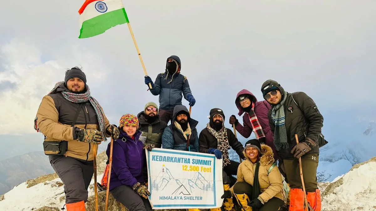 Himalaya Shelter trek group with the Indian flag and a Kedarkantha Summit 12,500 feet banner on the snowy summit in winter