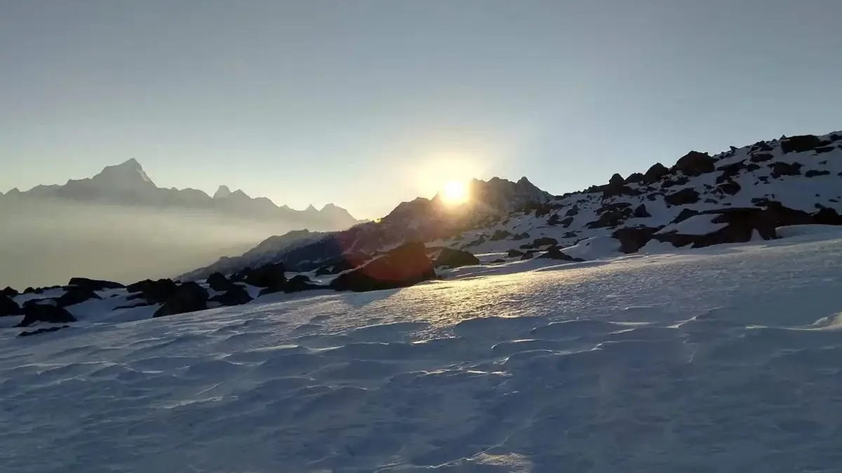 Sun rising behind a rocky snow ridge on the Brahmatal trek, with a line of Himalayan peaks on the left horizon