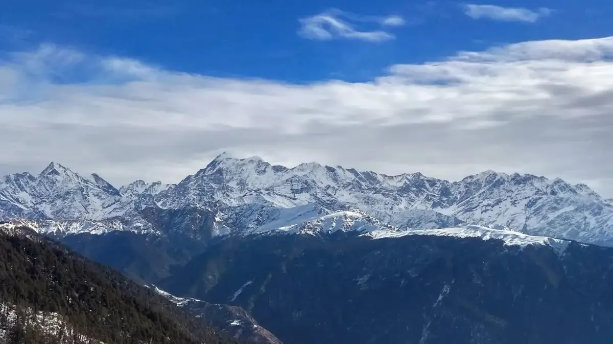 Snow-covered Himalayan peaks above forested ridges seen from the Brahmatal trail under a blue sky