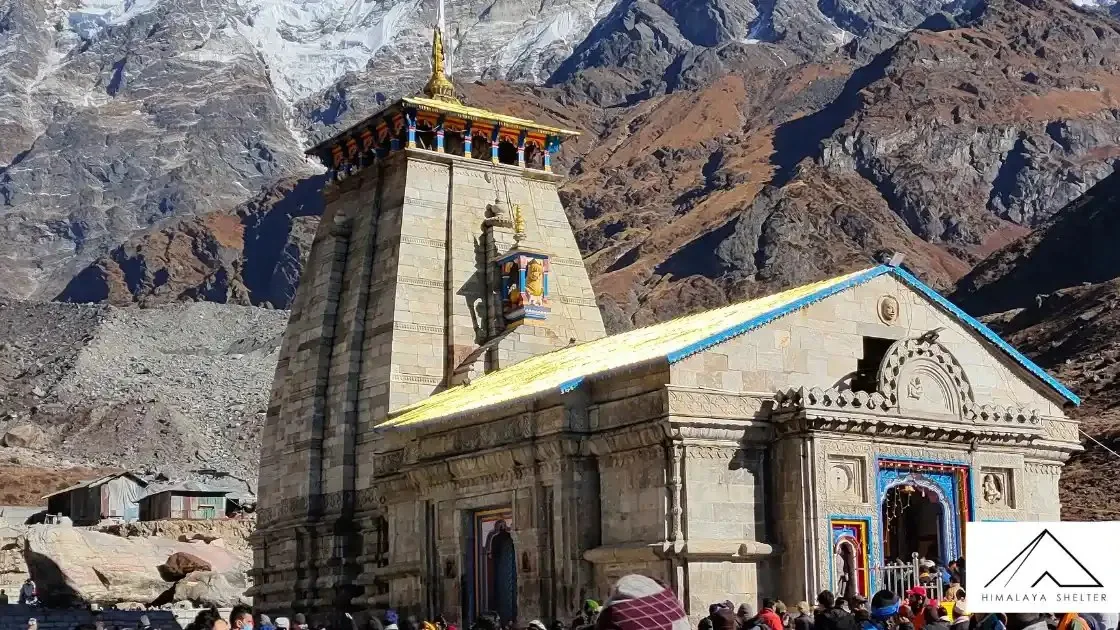Kedarnath temple with its stone spire and lit entrance, in front of steep snow-covered mountains